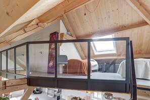 A loft-style bedroom with a sloped ceiling, a skylight, a bed, a chair, and a small table with a lamp.