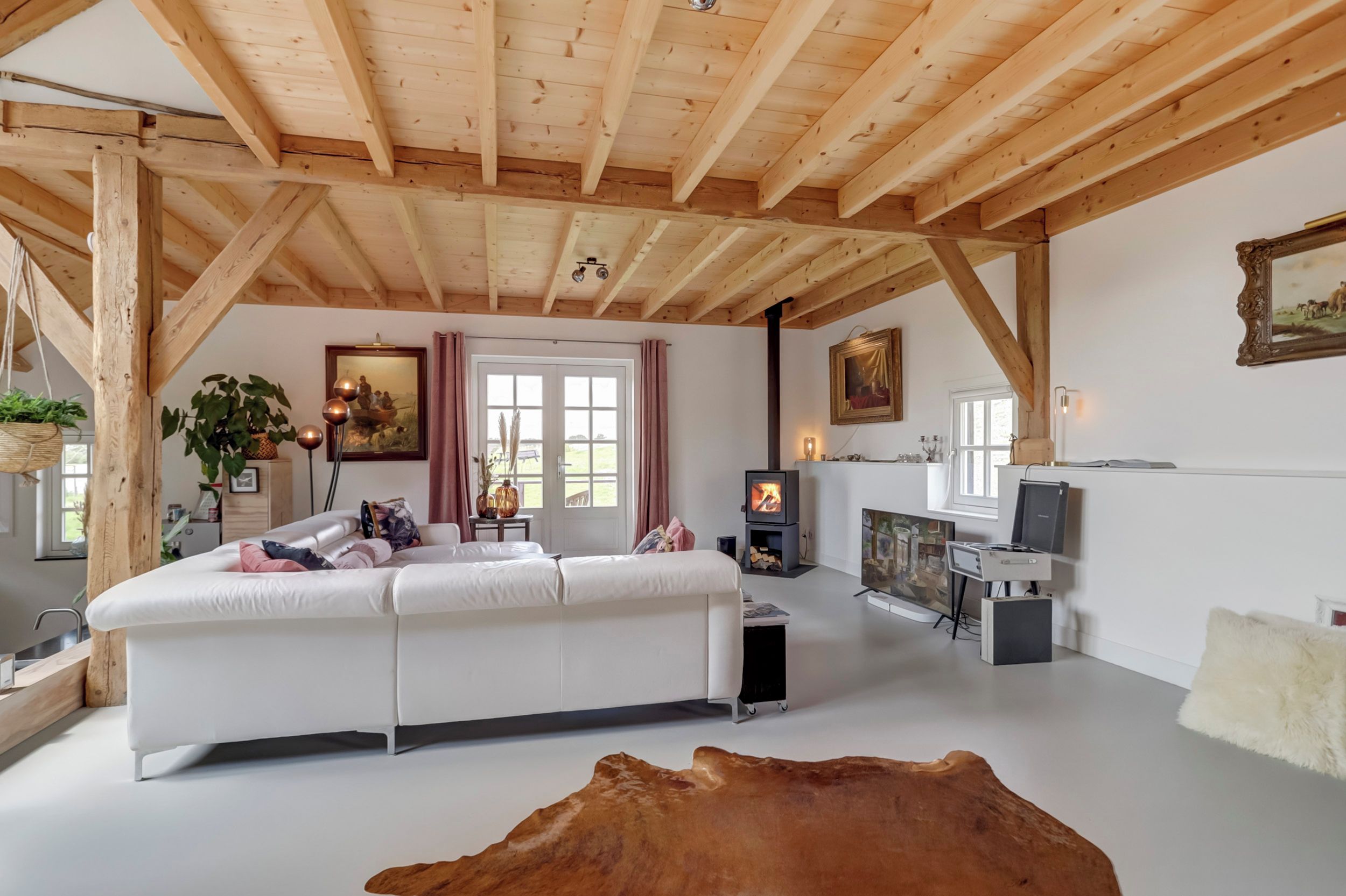 A spacious living room with a white sofa, wooden beams, a fireplace, and artwork on the walls.
