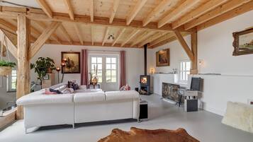A spacious living room with a white sofa, wooden beams, a fireplace, and artwork on the walls.