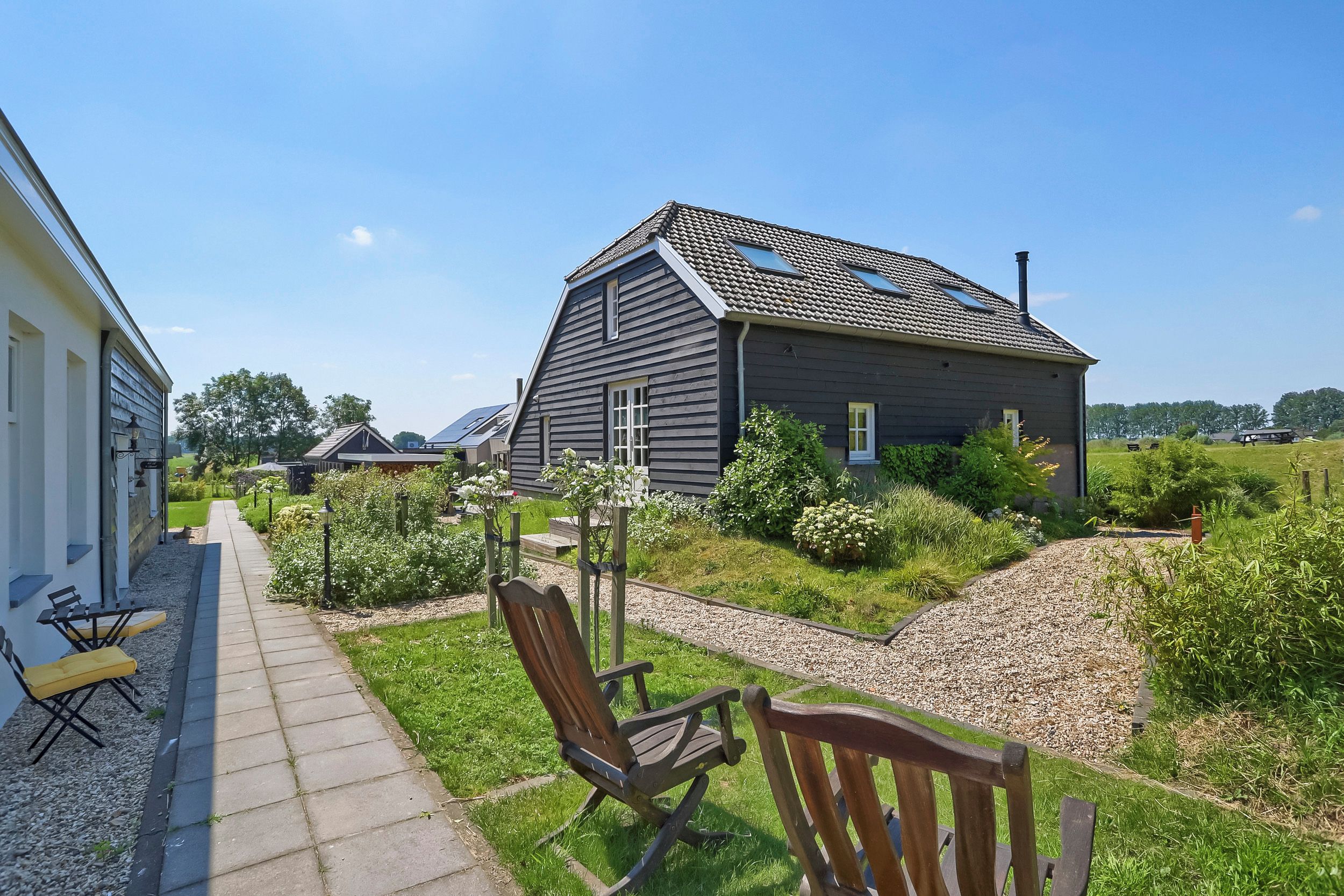 A residential property with a paved pathway, a wooden bench, and a garden area with various plants.