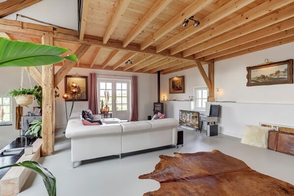 A modern living room with a white sofa, wooden beams, a leather rug, and a television.