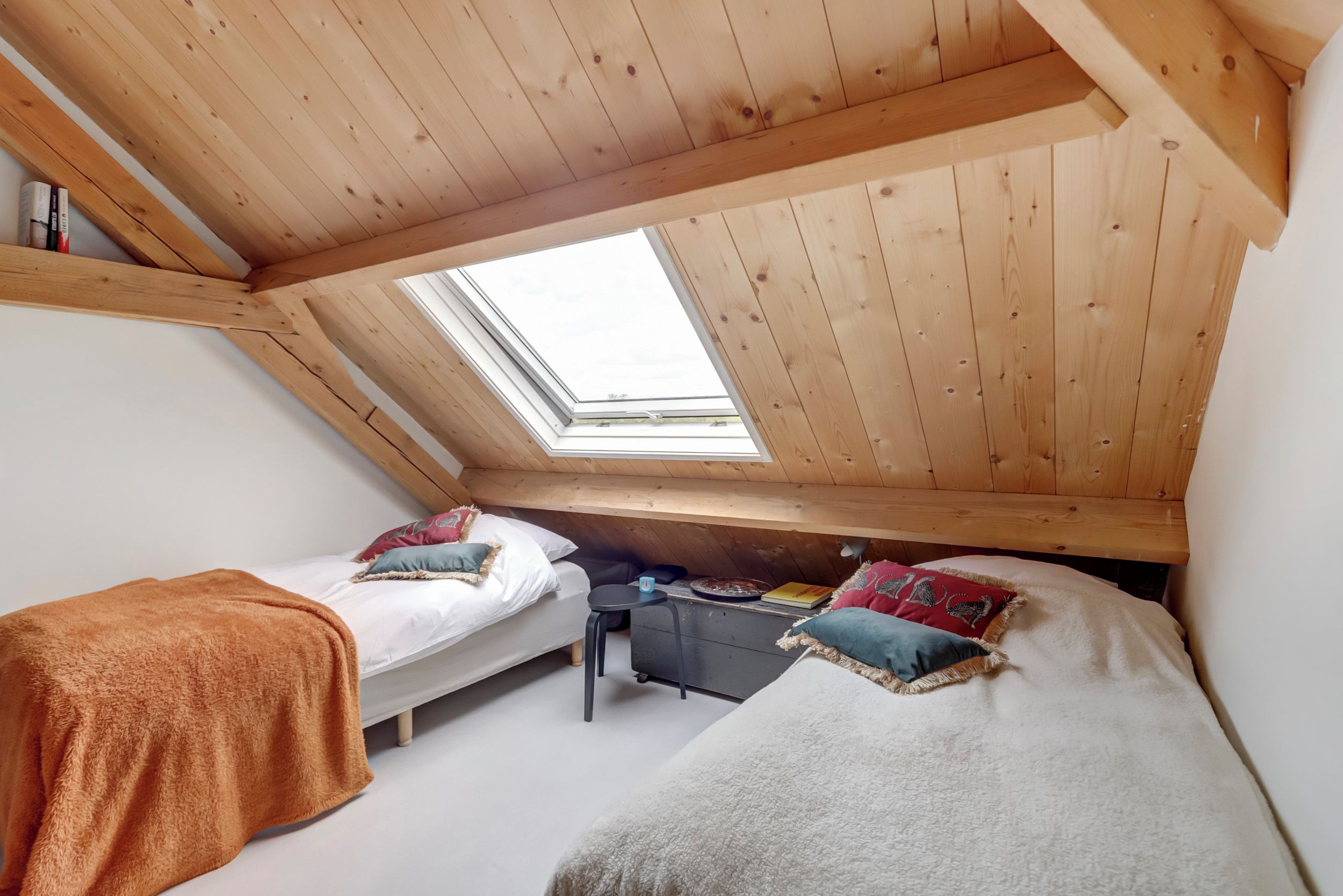 A dormitory room with two beds, a skylight, and a desk with a chair.