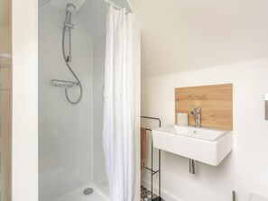 A modern bathroom with a glass-enclosed shower, a white sink with a wooden panel above it, and a towel rack. - 3 bedroom accommodation in Portmahomack (Portmahomack)
