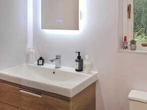 Une salle de bain avec un lavabo blanc, un miroir, une fenêtre donnant sur un beau paysage et une petite plante en pot.