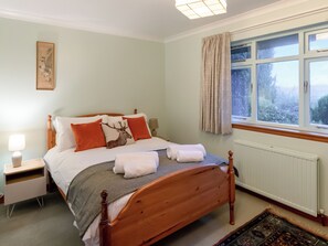 Une chambre à coucher avec un lit en bois, une table de chevet, une lampe, une fenêtre avec des rideaux et un radiateur.