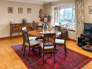 Un coin repas avec une table ronde en bois, quatre chaises, un tapis à motifs rouges, un téléviseur et une fenêtre avec des rideaux.