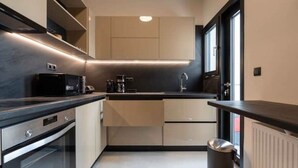 A modern kitchen with built-in appliances, a window, and a trash bin. - Corner penthouse in Acropolis (Athina)