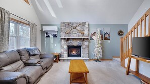 Una sala de estar con chimenea de piedra, un sofá de cuero, una mesa de centro de madera y un mueble para televisor.