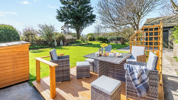 An outdoor patio with wicker furniture, a wooden deck, and a view of a garden and trees. - 3 bedroom accommodation in Silecroft, near Millom (Silecroft, near Millom)