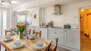 A modern kitchen with white cabinetry, a dining table set for four, and a view into the adjacent dining area. - 3 bedroom accommodation in Silecroft, near Millom (Silecroft, near Millom)