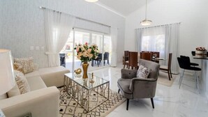 A spacious living room with a sofa, armchair, and coffee table, a dining area with chairs, and a kitchen area with a dining table and chairs. - Villa Paradise Punta Cana (Punta Cana)