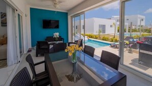 A modern living room with a pool view, a flat-screen TV mounted on the wall, and a dining area with a table and chairs. - Villa Paradise Punta Cana (Punta Cana)