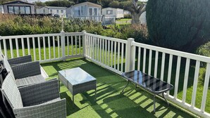 Un espace patio agrémenté d’une clôture blanche, d’un gazon synthétique et de mobilier d’extérieur comprenant une table et des chaises.