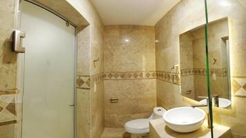 Un baño con cabina de ducha de vidrio, inodoro y lavamanos con espejo.