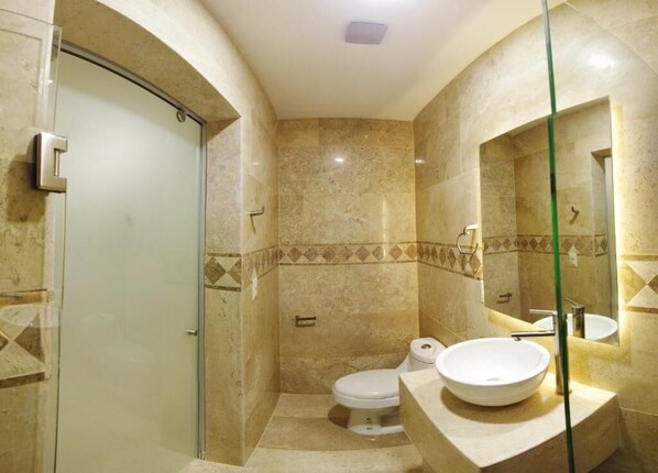 Un baño con cabina de ducha de vidrio, inodoro y lavamanos con espejo.