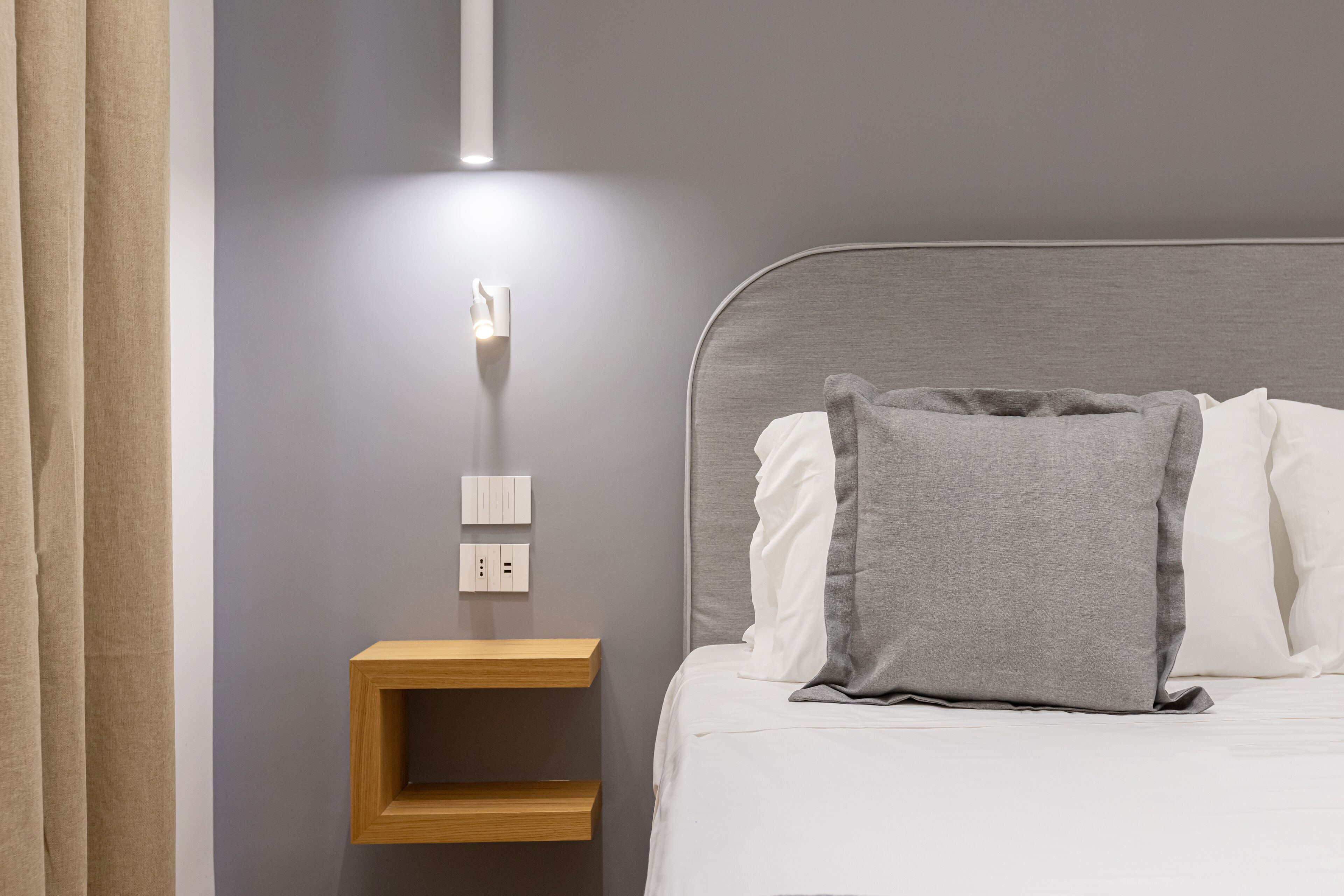 A neatly made bed with a grey pillow and a wooden nightstand beside it.