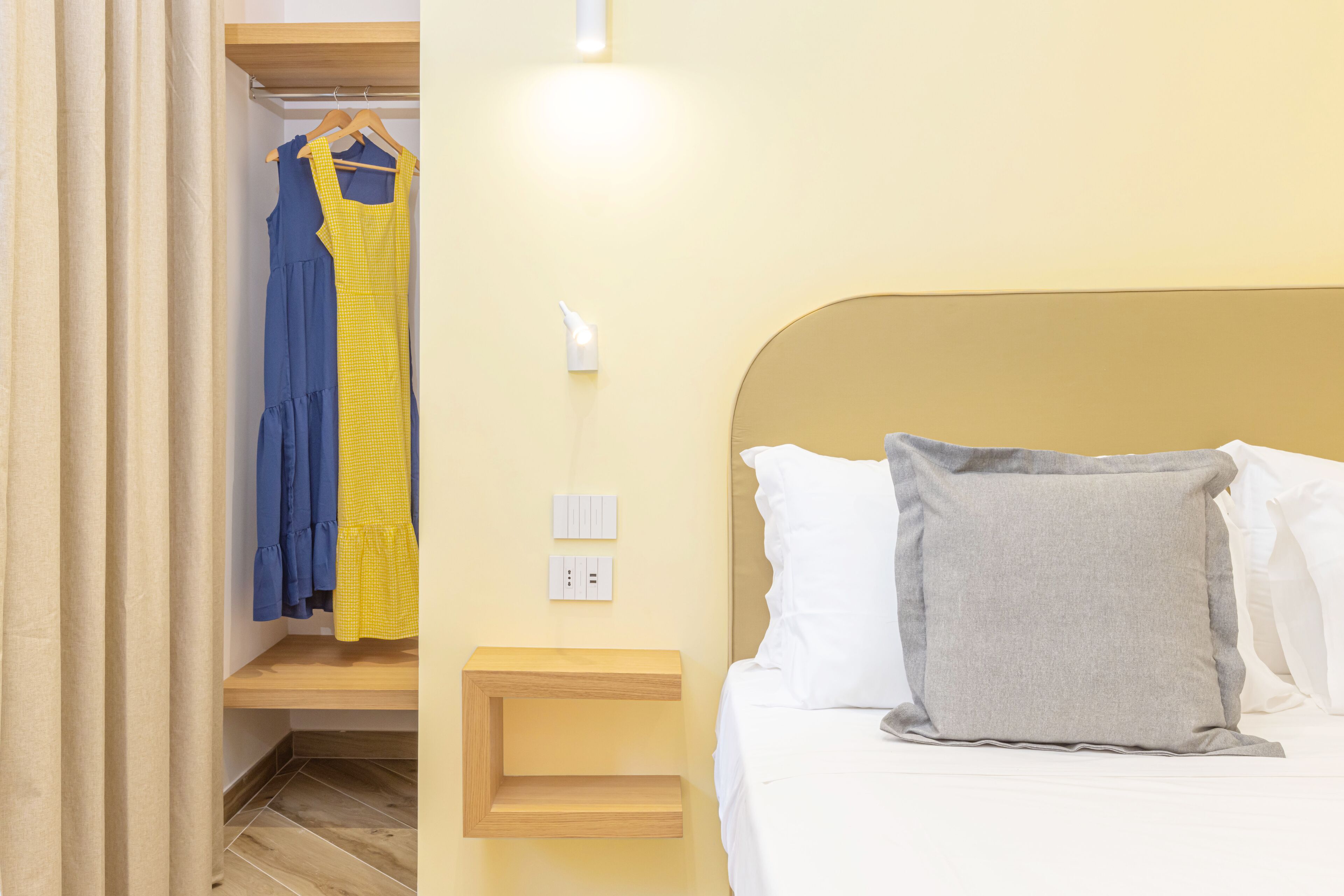 Camera da letto con un letto, un comodino, una presa a muro e un armadio con abiti appesi.