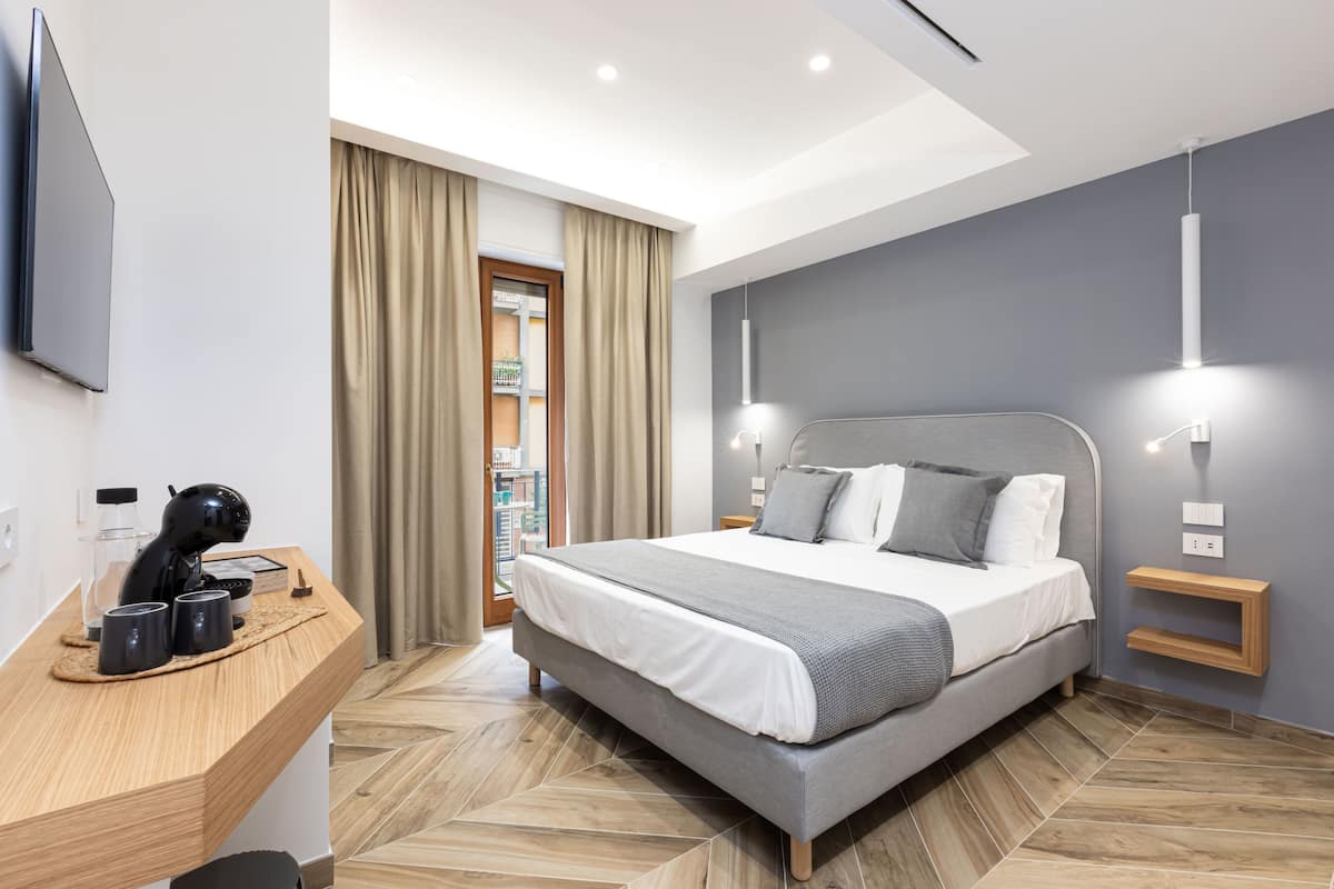 A modern hotel room with a large bed, a desk with a coffee maker, and a TV mounted on the wall.