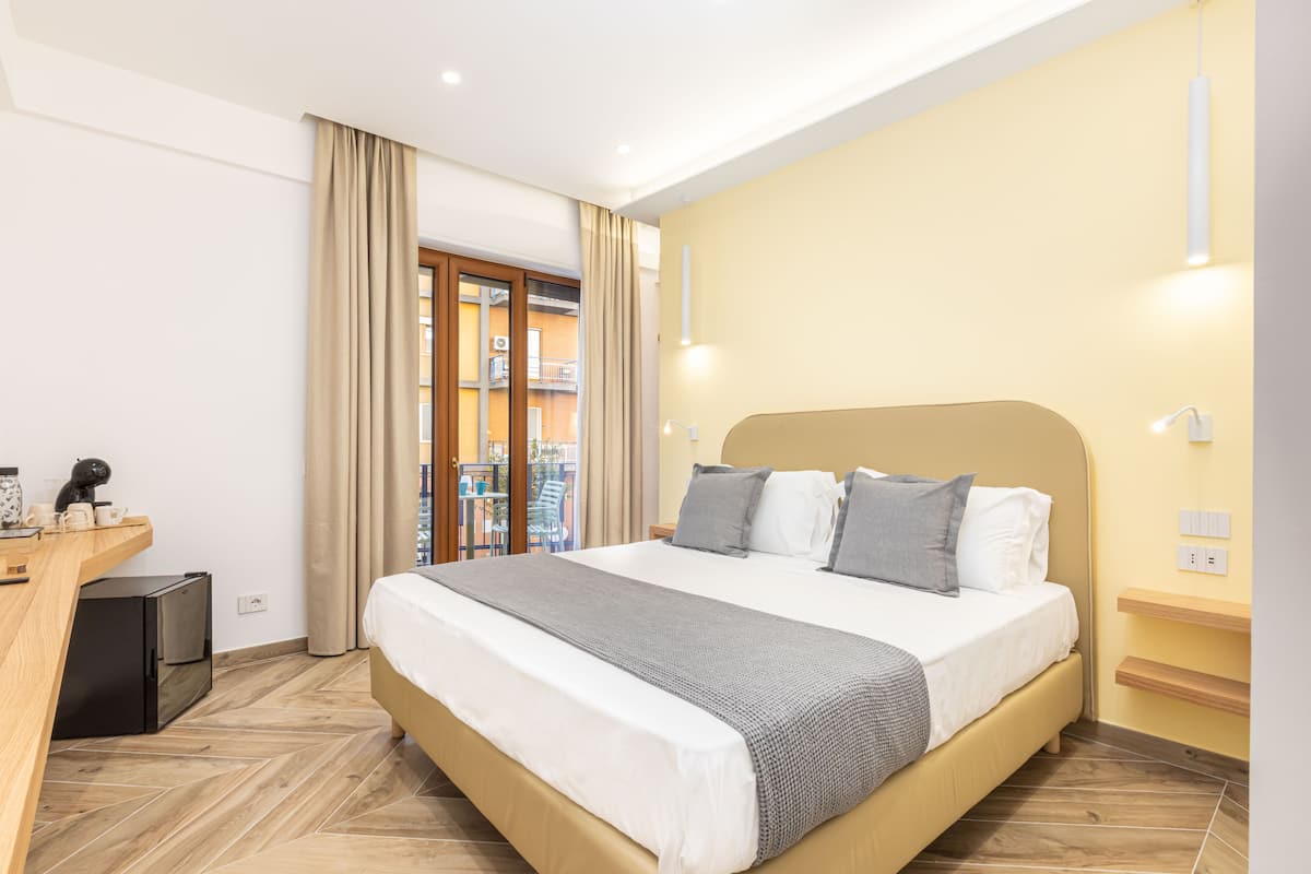 A modern hotel room with a large bed, a desk, and a view of the outside balcony.