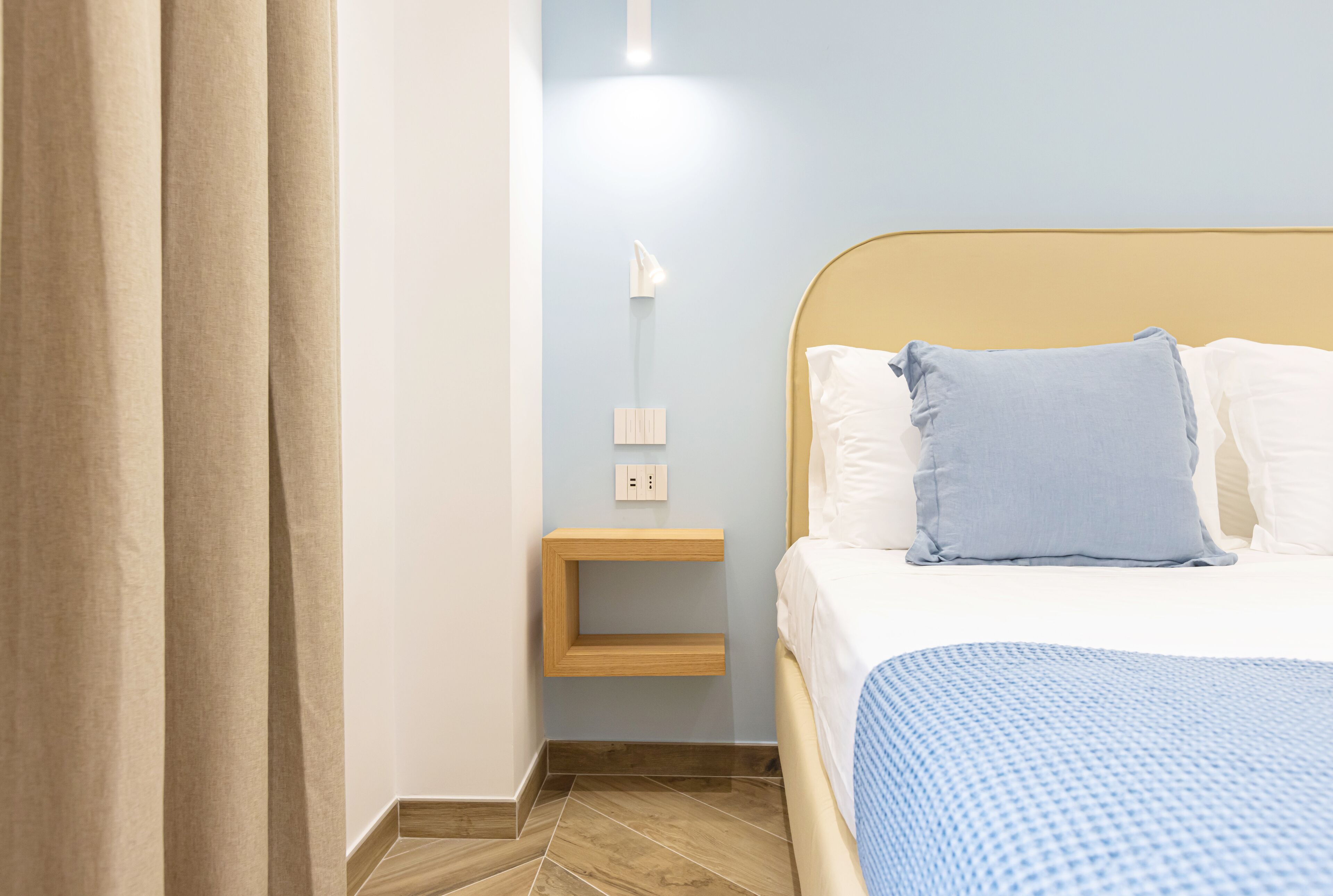 A neatly arranged bedroom with a bed, a bedside table, a wall-mounted light, and a curtain.