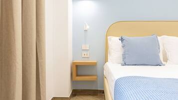 A neatly arranged bedroom with a bed, a bedside table, a wall-mounted light, and a curtain.