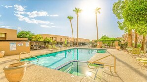 A swimming pool with a sunlit sky, palm trees, and a fenced area with lounge chairs. - North Mountain Townhouse (Phoenix)