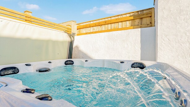 Un bain à remous avec une terrasse en bois et un mur blanc en arrière-plan.