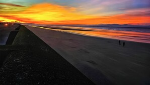 Une plage au coucher du soleil, une route et quelques personnes qui se promènent.