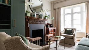 A living room with a fireplace, a bookshelf, and a large window with curtains. - Burton Mews by onefinestay (London)