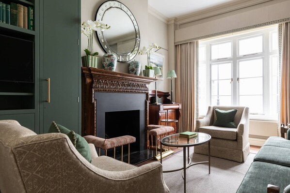 A living room with a fireplace, a bookshelf, and a large window with curtains.