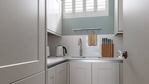 A kitchen with white cabinets, a wooden countertop, a window with blinds, and a knife block. - Burton Mews by onefinestay (London)