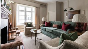 A living room with a green sofa, armchairs, a coffee table, and a fireplace. - Burton Mews by onefinestay (London)
