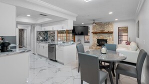 A modern kitchen with a central island, a dining area with a round table and chairs, and a stone fireplace. - New Luxury House Pool. Just 14 Minutes From the Airport (Tampa)