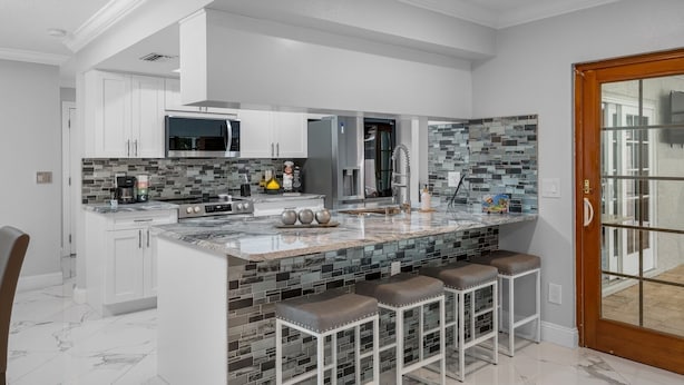 A modern kitchen with white cabinetry, a granite countertop, and a mosaic backsplash. - New Luxury House Pool. Just 14 Minutes From the Airport (Tampa)