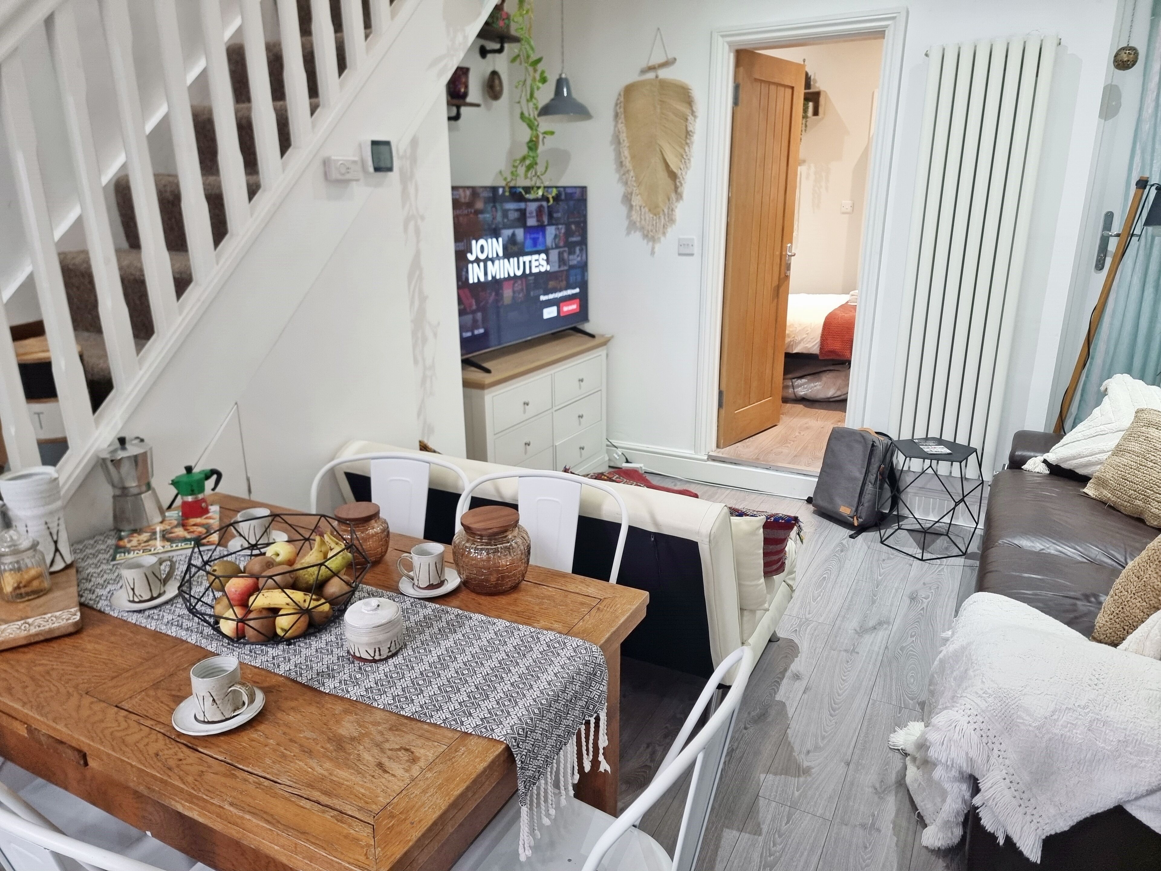 Un salon chaleureux avec une table à manger en bois, mise pour quatre personnes, un canapé confortable et un téléviseur en arrière-plan.