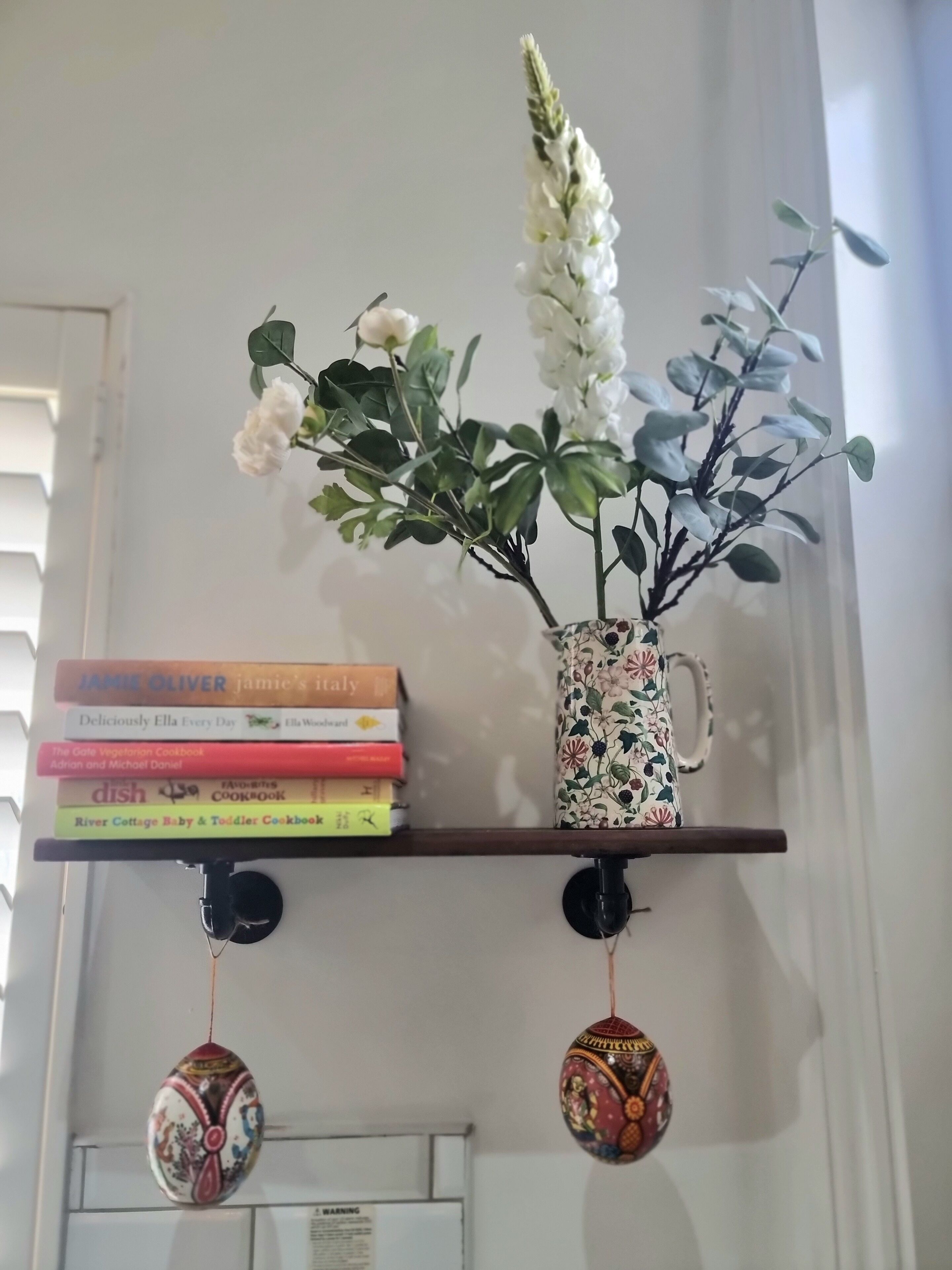 A bookshelf with books and a floral vase.