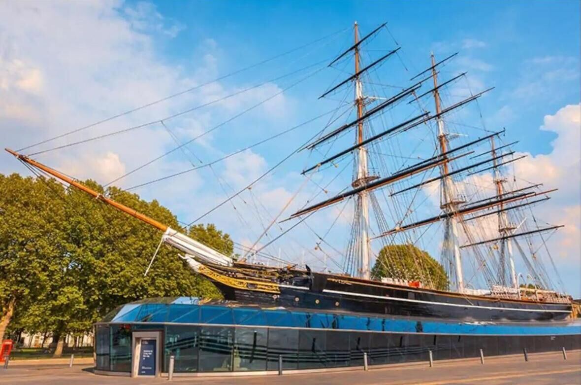 Un grand voilier était amarré dans un port de plaisance moderne, à proximité d’un bâtiment en verre.