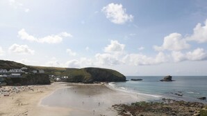 A coastal beach with a sandy shore, a few buildings, and a rocky outcrop in the distance. - Beachspoke Loft (Redruth)