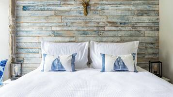A bed with white bedding and striped pillows, a rustic wooden headboard, and a mounted deer head.