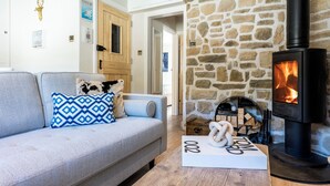 A cozy living room with a stone fireplace, a sofa with patterned cushions, and a wooden coffee table. - Beachspoke Loft (Redruth)