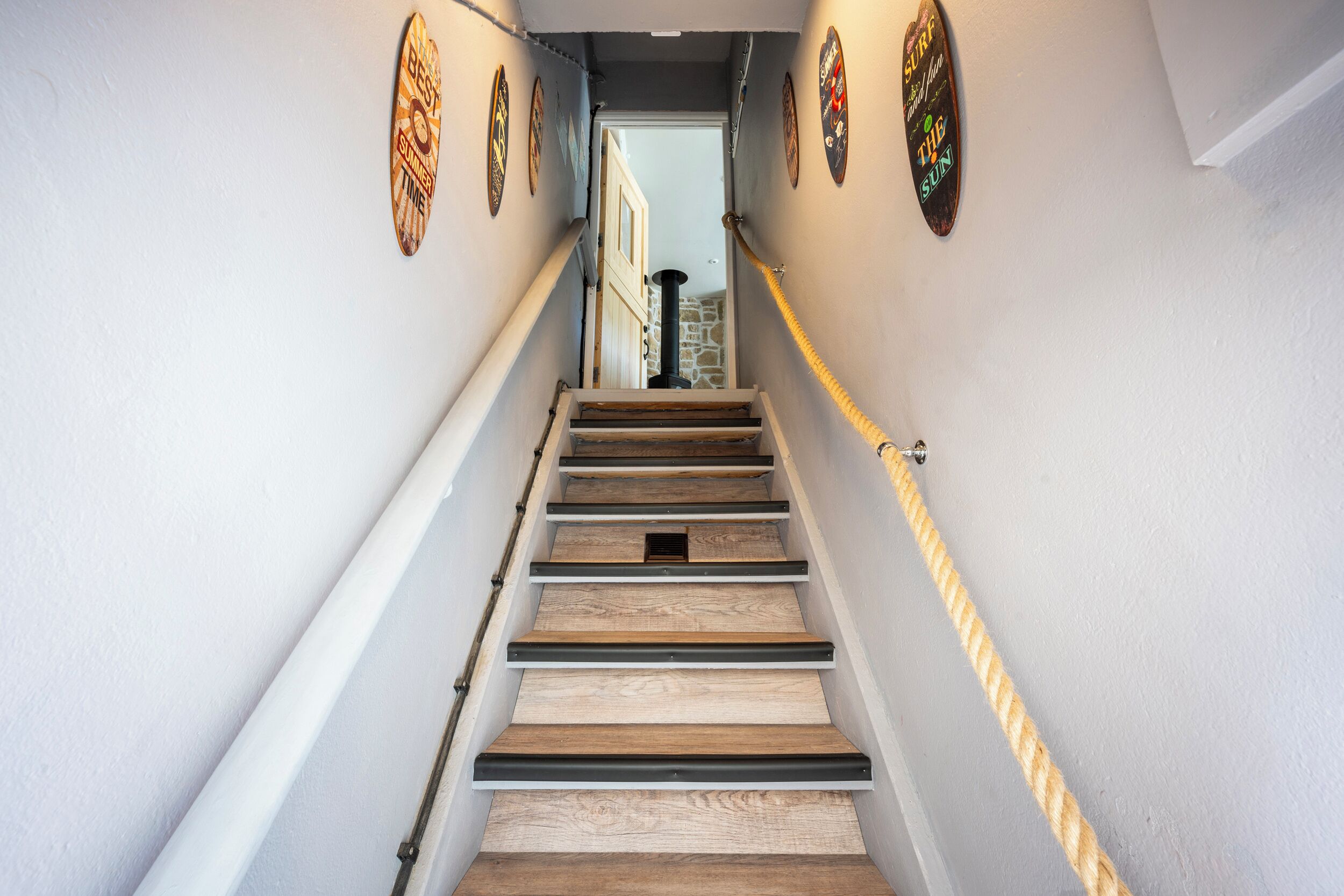 Eine Holztreppe mit Seilgeländer, weißen Wänden und Wandverzierungen.