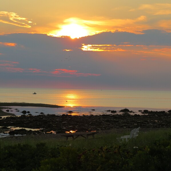 A sunset over a rocky shoreline with a wooden pier and a boat in the distance.