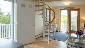 Una escalera de caracol conduce a un segundo piso, una mesa de vidrio con un jarrón de flores y una puerta con la leyenda "EAST SANDWICH BEACH".