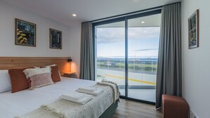 A modern hotel room with a large bed, a view of the sea, and a balcony with a railing. - Casa ProMar - Sea View Serenity (Ponta Delgada)