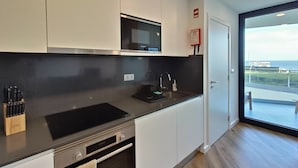 A modern kitchen with white cabinets, a Bosch microwave, and a black countertop. There's a window with a view of the sea and a door leading to a balcony. - Casa ProMar - Sea View Serenity (Ponta Delgada)
