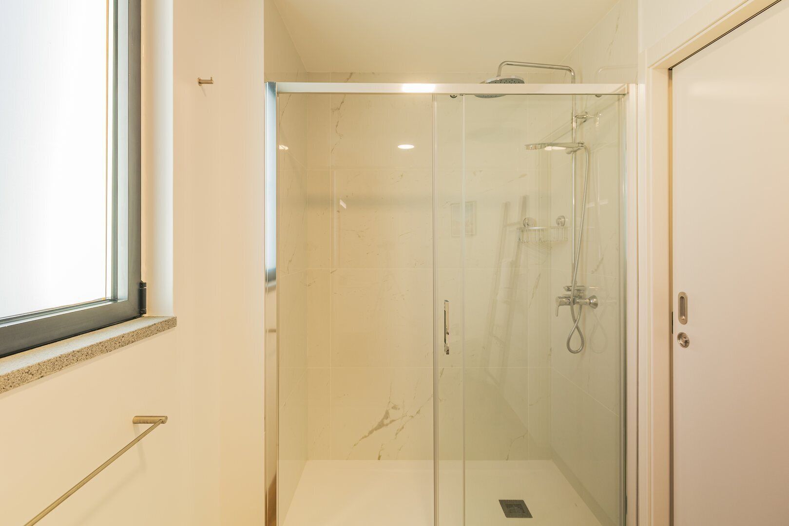 A glass-enclosed shower with a handheld showerhead and a wall-mounted faucet.