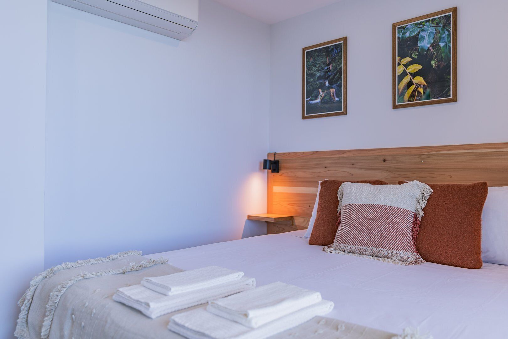 A bedroom with a bed, two framed pictures, a nightstand, and a wall-mounted air conditioner.