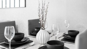A dining table set with black bowls, plates, and wine glasses, accompanied by a white vase with branches. - Hotel Comforts & Home Conveniences -sleeps 8 (Birmingham)