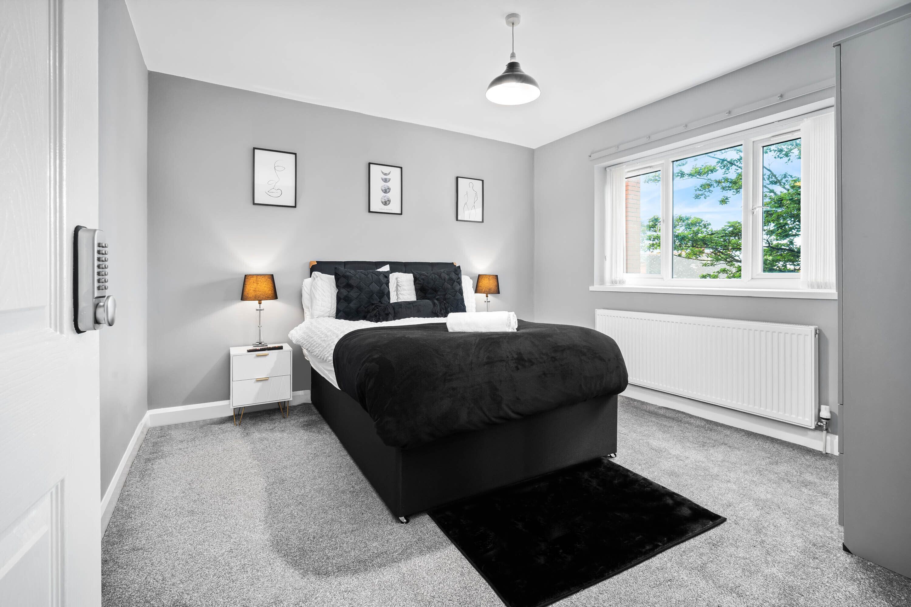 A bedroom with a black bed, white nightstands, a black rug, and a window with a view of trees.