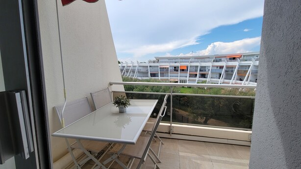A balcony with a table and chairs, a potted plant, and a view of a modern building complex.